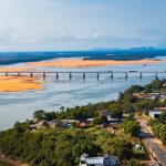 Vista aérea de uma ponte atravessando um rio cercado por vegetação, em Boa Vista (RR).