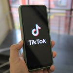 Mão segura um smartphone com a tela do aplicativo TikTok aberta em um ambiente interno.