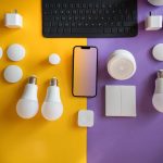 Vista superior de dispositivos eletrônicos e acessórios de casa inteligente dispostos sobre um fundo colorido.