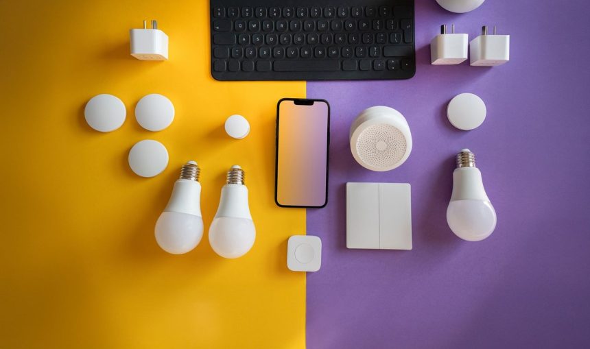 Vista superior de dispositivos eletrônicos e acessórios de casa inteligente dispostos sobre um fundo colorido.
