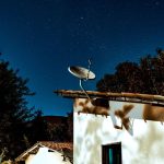 Casa rural à noite, sob um céu estrelado, com uma antena parabólica instalada ao lado.