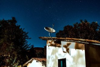 Casa rural à noite, sob um céu estrelado, com uma antena parabólica instalada ao lado.