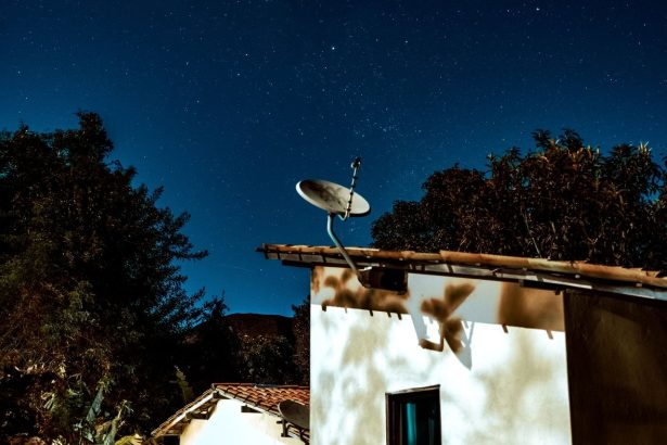 Casa rural à noite, sob um céu estrelado, com uma antena parabólica instalada ao lado.