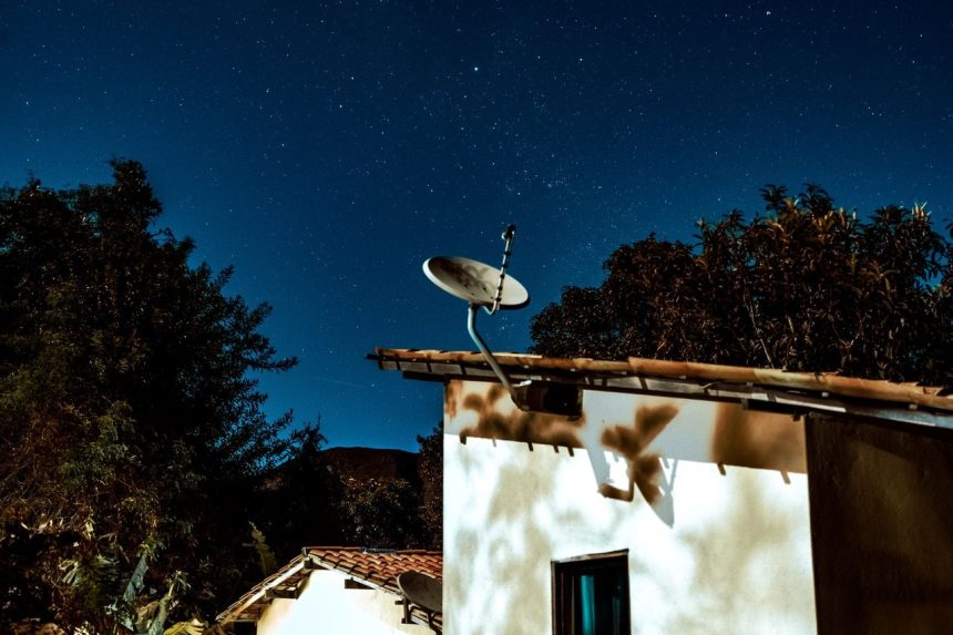 Casa rural à noite, sob um céu estrelado, com uma antena parabólica instalada ao lado.