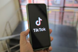 Mão segura um smartphone com a tela do aplicativo TikTok aberta em um ambiente interno.