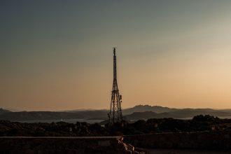 Torre de telecomunicações em silhueta diante de uma paisagem rural montanhosa ao entardecer