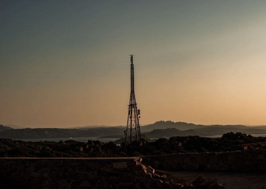 Torre de telecomunicações em silhueta diante de uma paisagem rural montanhosa ao entardecer