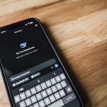 Smartphone exibindo a interface de um aplicativo de mensagens sobre uma mesa de madeira.