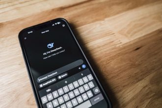 Smartphone exibindo a interface de um aplicativo de mensagens sobre uma mesa de madeira.